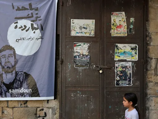 A Palestinian girl stands near a poster of Ibrahim al-Nabulsi, a commander of the Al-Aqsa Martyrs' Brigade, one of the main terrorist groups present in the West Bank operating under the ruling Fatah party, who was killed by Israeli troops in August 2022. The poster bears the Samidoun logo